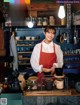 A woman in an apron standing behind a counter in a kitchen.