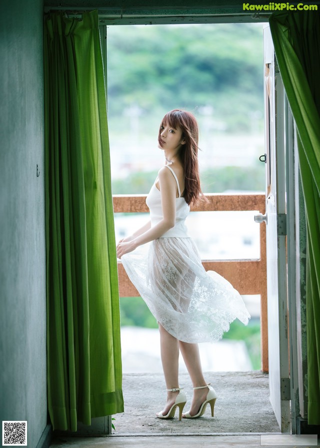 A woman in a white dress standing by a window.