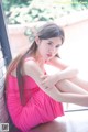 A woman in a pink dress sitting on a window sill.