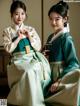 A couple of women in hanbok sitting next to each other.