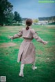 A woman in a trench coat and white boots standing in a field.